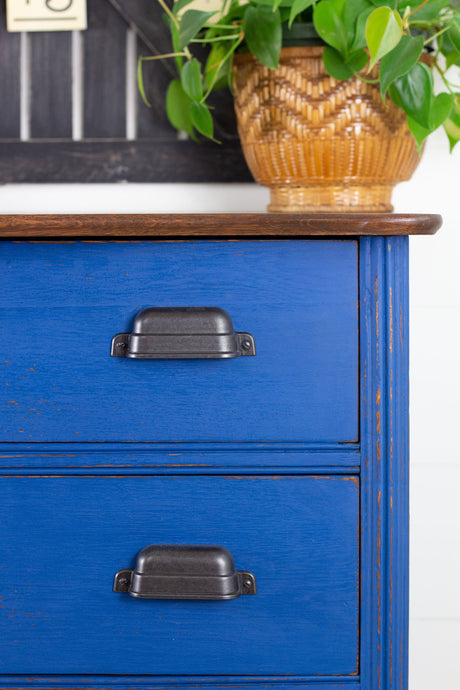 Two drawers on a blue dresser painted in Homestead House Ocean Milk Paint, with a potted plant on top.