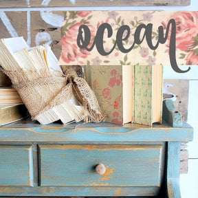Blue wooden shelf painted in Old Fashioned Milk Paint Ocean, shown with books, twine, and a floral “ocean” sign.