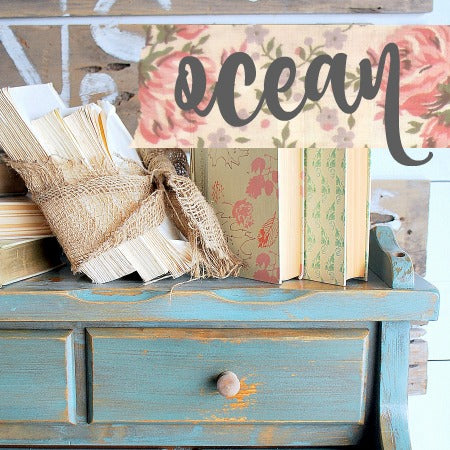Blue wooden shelf painted in Old Fashioned Milk Paint Ocean, shown with books, twine, and a floral “ocean” sign.