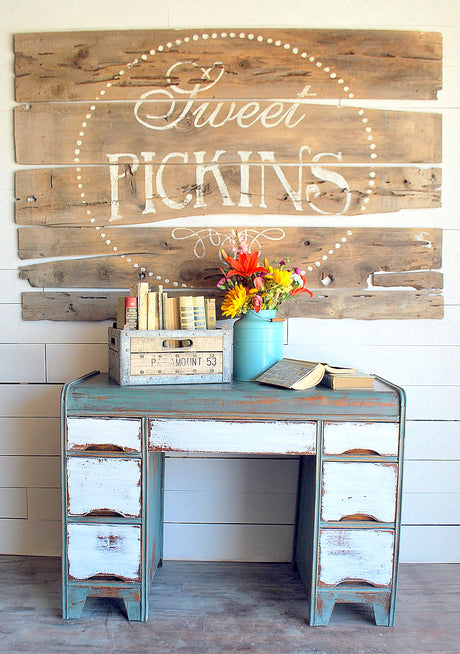 Vintage desk with books, flowers, and crate beneath Old Fashioned Milk Paint “Ocean” sign by Sweet Pickins.