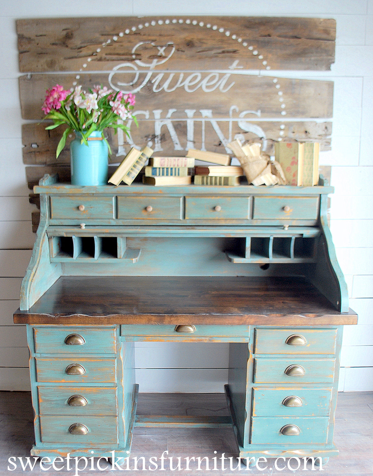 Blue-green wooden desk painted with Ocean by Old Fashioned Milk Paint, brass handles, blue vase with flowers, and books.