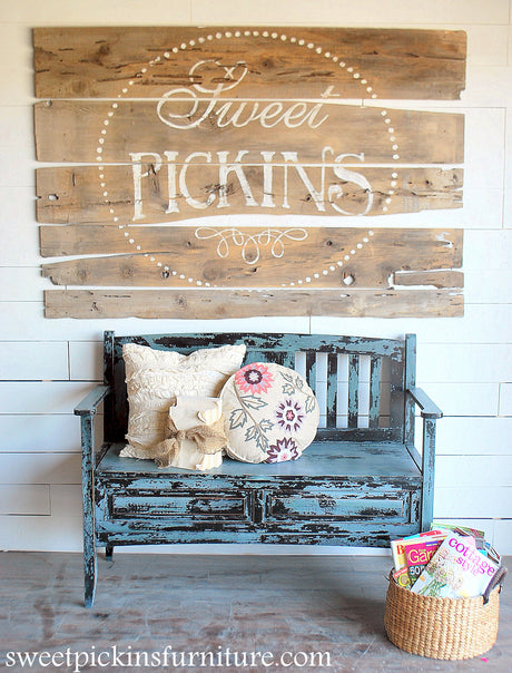 Blue bench painted in Ocean by Old Fashioned Milk Paint, below a Sweet Pickins sign with a nearby basket of magazines.