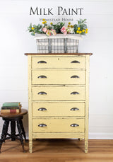 Yellow Ochre Milk Paint dresser by Homestead House next to a stool stacked with books and topped with flowers.