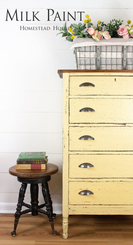 Yellow dresser in Ochre Milk Paint by Homestead House, shown with stool, books, flowers, and branded wall art.