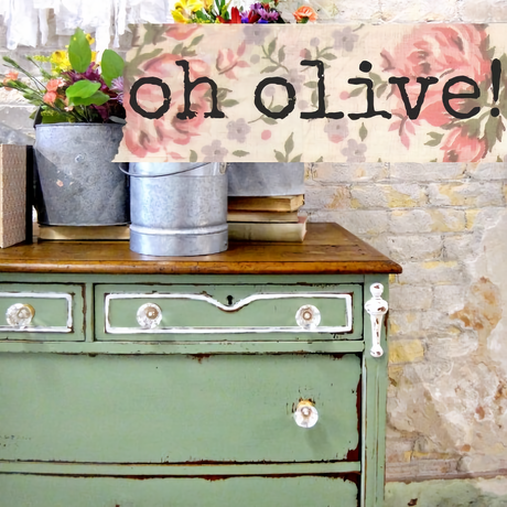 Dresser in Old Fashioned Milk Paint “Oh Olive!” with metal bucket of flowers beside a floral sign.