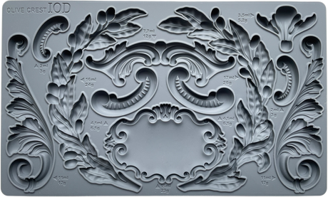 Olive Crest Mould by IOD in gray silicone featuring ornate leaf, scroll designs, and measurement markings.