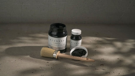 Onyx Alchemy Paint by Fusion Mineral Paint shown in a jar, small bottle, open lid, and wooden-handled brush beside them.