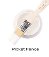 Brush with white paint rests on open Fusion Mineral Paint jar labeled “Picket Fence.”.
