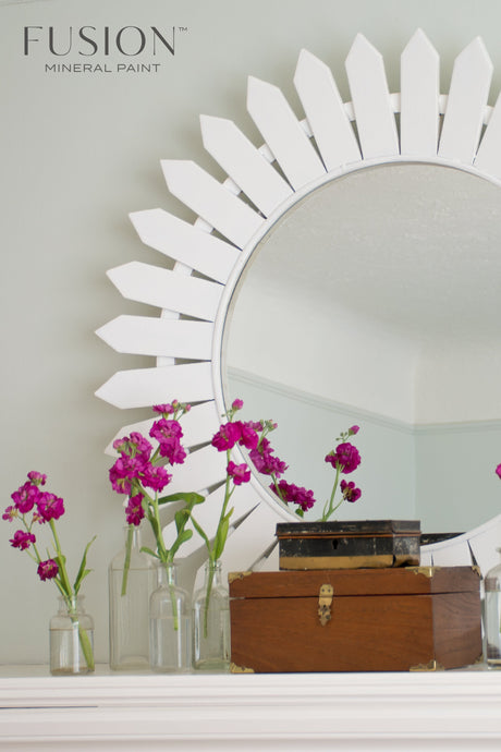 Round mirror with Picket Fence Fusion Mineral Paint sunburst frame, pink flowers in jars, and wooden box.