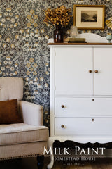 White cabinet in Porcelain Milk Paint by Homestead House next to beige armchair and floral wallpaper.