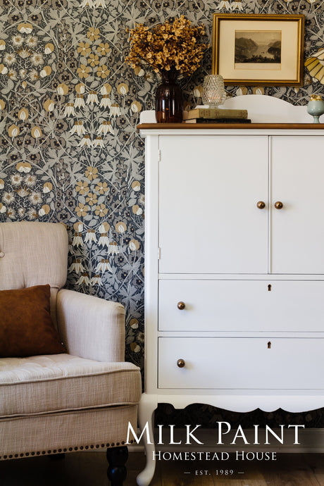 White cabinet in Porcelain Milk Paint by Homestead House next to beige armchair and floral wallpaper.