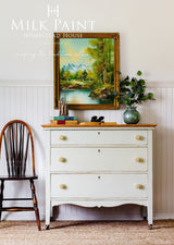 White dresser with wooden top in PotPourri Milk Paint by Homestead House, shown with books and a small vase.