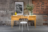 Yellow desk painted in Homestead House Prairie Sunset Milk Paint with a white chair, vase, and framed photo.