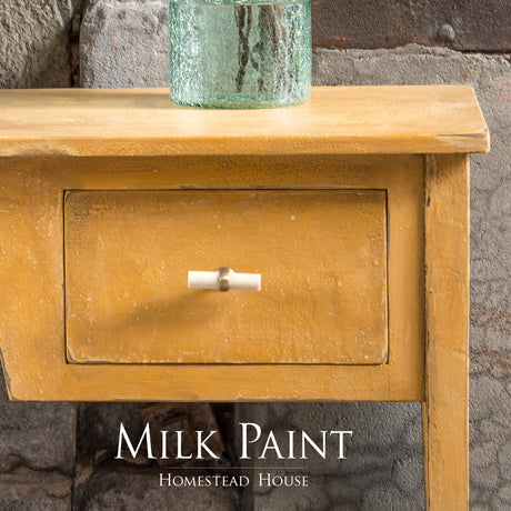 Yellow wooden table painted in Prairie Sunset Milk Paint with drawer, glass vase, and visible Homestead House branding.