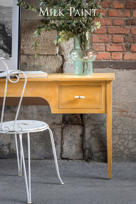 Vintage desk in Prairie Sunset Milk Paint by Homestead House with white chair and green vase.