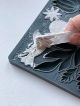 Hand lifting white plaster shape from Primitive Mould by IOD, featuring raised leaf and flower patterns.