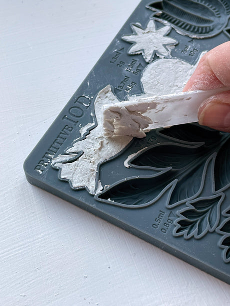 Hand lifting white plaster shape from Primitive Mould by IOD, featuring raised leaf and flower patterns.