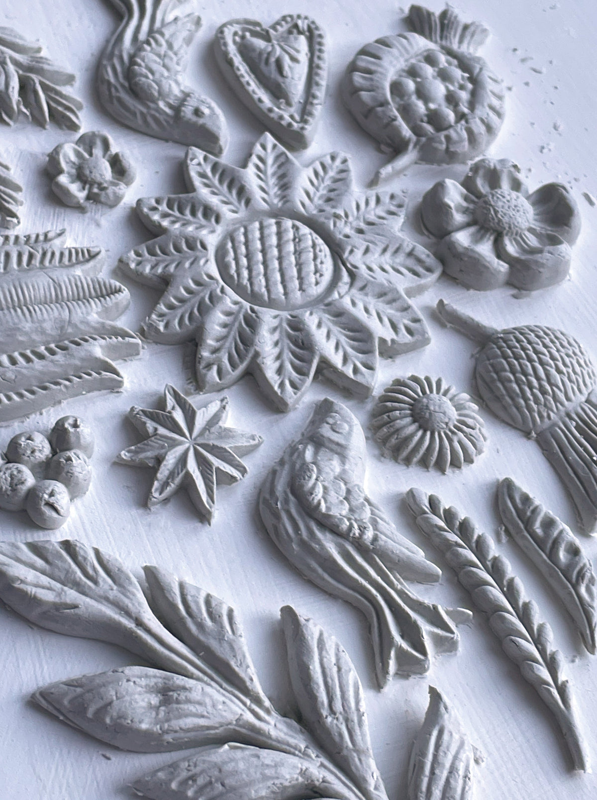 White clay shapes made with I.O.D. Primitive Mould, displaying flowers, leaves, and geometric patterns.