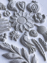 White clay shapes made with I.O.D. Primitive Mould, displaying flowers, leaves, and geometric patterns.