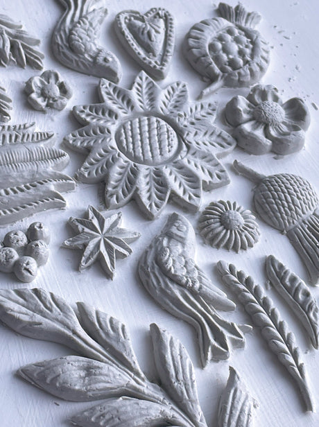White clay shapes made with I.O.D. Primitive Mould, displaying flowers, leaves, and geometric patterns.