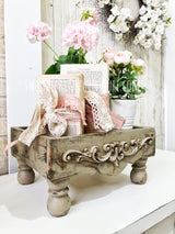 Distressed Old Fashioned Milk Paint stand with lace-tied books and a white pot of pink flowers.