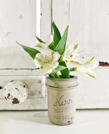 White lilies with green leaves arranged in a mason jar painted Proper by Old Fashioned Milk Paint, on a white cabinet.
