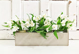 White blooms in jars arranged in a beige box; rustic wall painted with Proper by Old Fashioned Milk Paint behind.