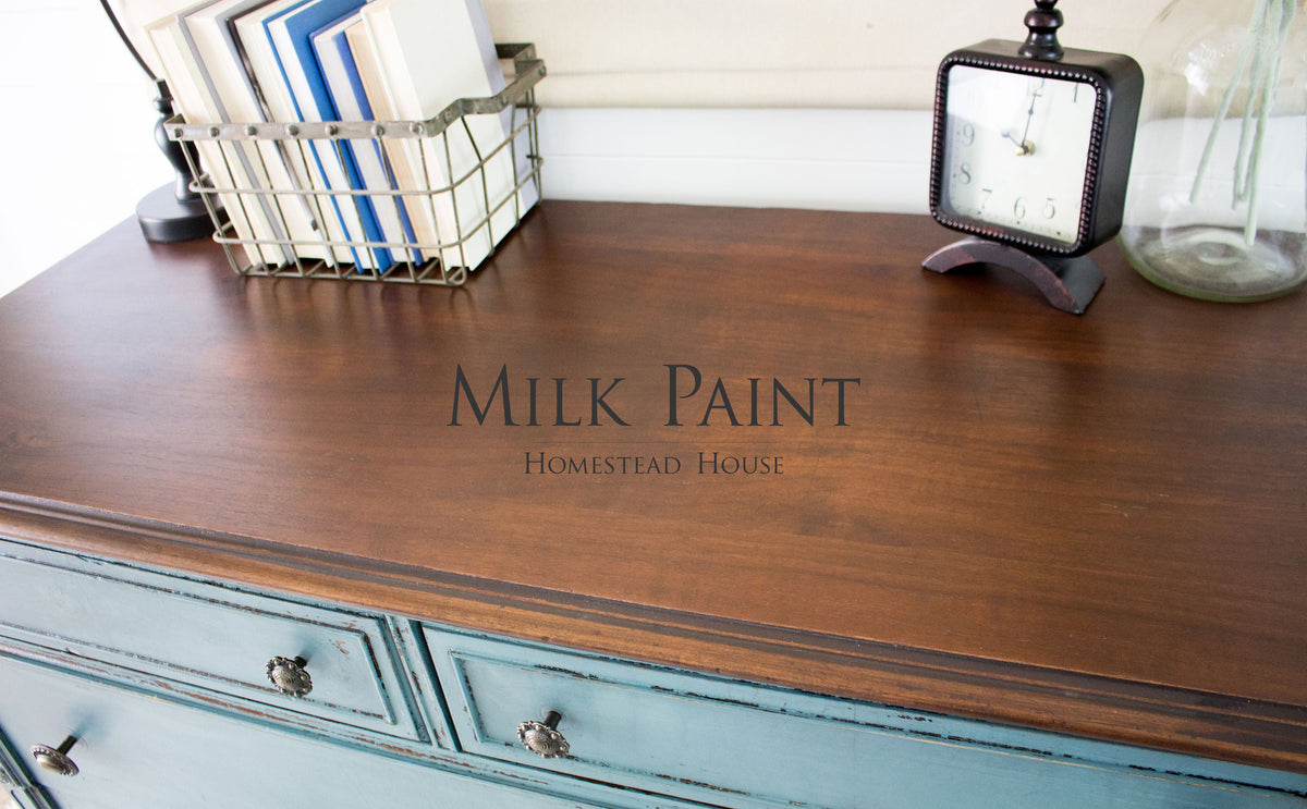 Dresser with drawers in Quaker Blue Milk Paint by Homestead House, shown with clock, basket of books, and jug.