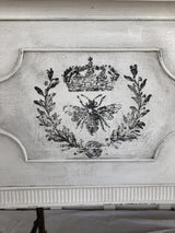 Black crown, laurel, and bee design from Queen Bee Stamp by IOD on distressed white wood background.