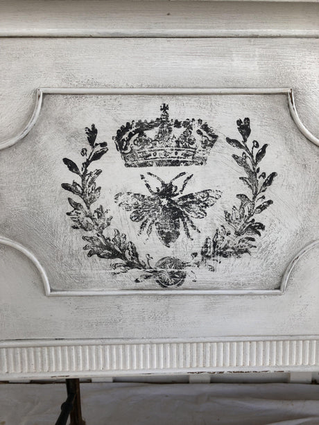 Black crown, laurel, and bee design from Queen Bee Stamp by IOD on distressed white wood background.