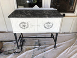 White cabinet with black legs, marble top, and I.O.D. Queen Bee Stamp detail.