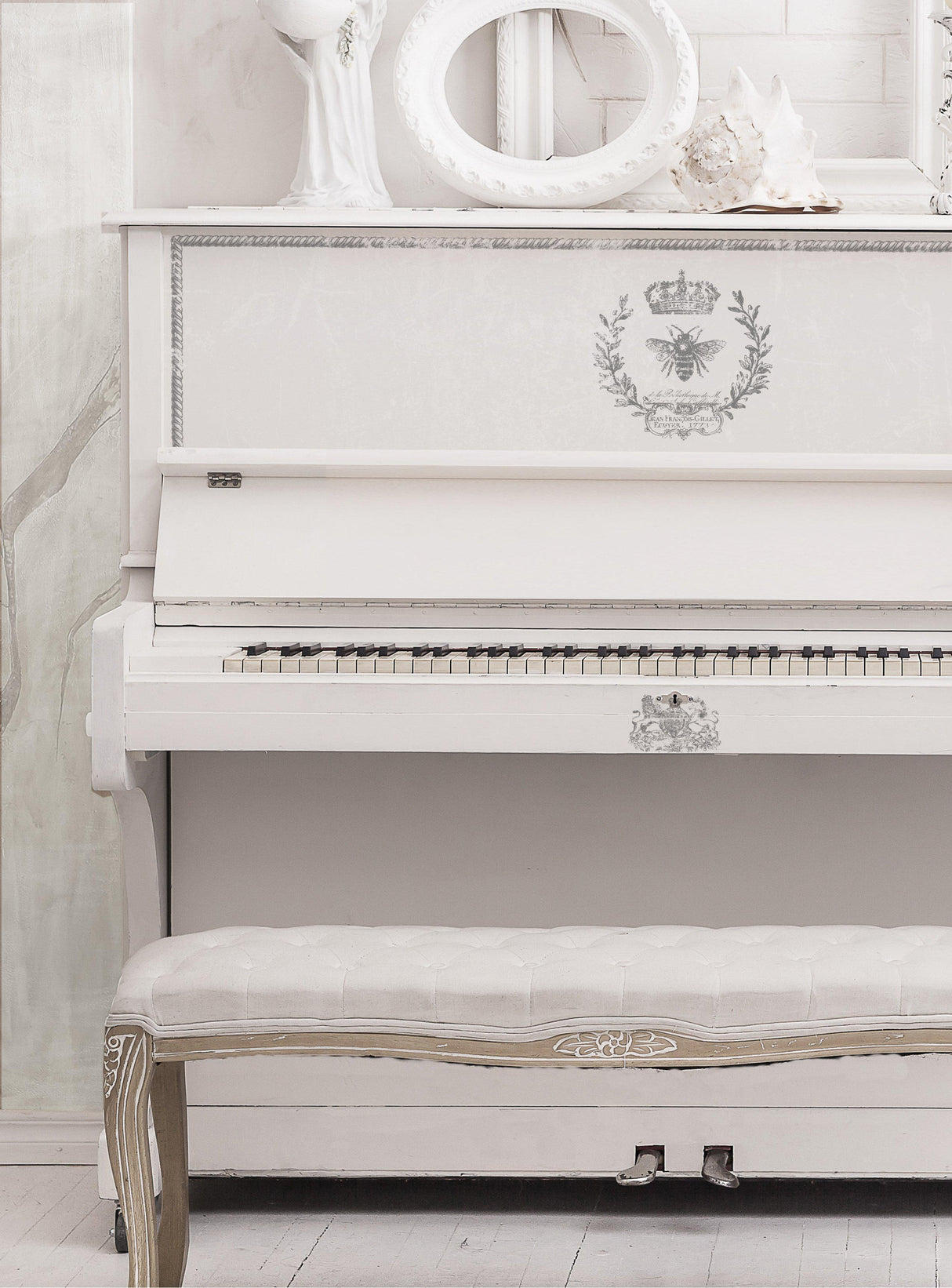 White upright piano with I.O.D. Queen Bee Stamp motifs, matching bench, and white decor on top.