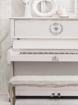 White upright piano with I.O.D. Queen Bee Stamp motifs, matching bench, and white decor on top.