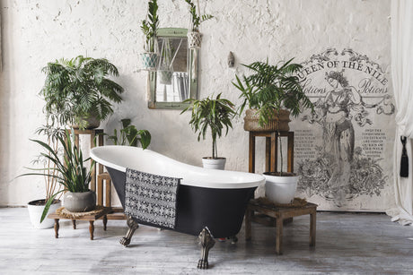Black clawfoot tub in rustic room with Queen of the Nile Paint Inlay by I.O.D., plants, and a towel nearby.
