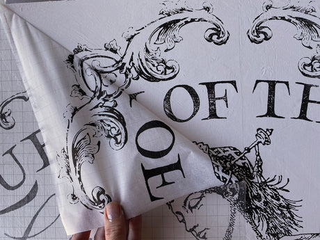 Hand peeling transfer paper from I.O.D. Queen of the Nile Paint Inlay floral and text design on white surface.