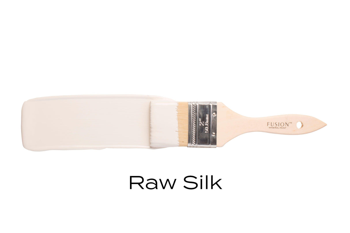 Brush with Fusion Mineral Paint Raw Silk, warm white acrylic paint, displayed on a plain white background.