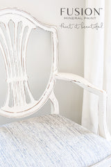 Distressed white chair with light blue seat, painted in Raw Silk by Fusion Mineral Paint, logo above.