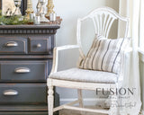 Distressed white armchair with striped cushion next to dresser in Raw Silk Fusion Mineral Paint warm white.