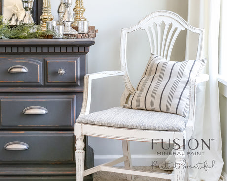 Distressed white armchair with striped cushion next to dresser in Raw Silk Fusion Mineral Paint warm white.