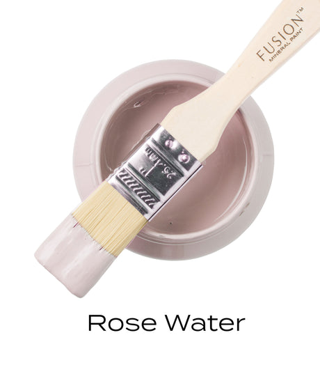 Paintbrush with pink paint resting on Fusion Mineral Paint Rose Water jar, viewed from above.