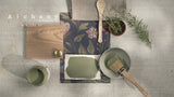 Rosemary Alchemy Paint by Fusion Mineral Paint with brush, wood sample, and paper on gray surface.