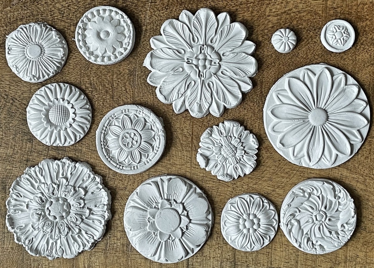 Thirteen round white clay Rosettes Mould medallions by IOD arranged on a wooden surface.