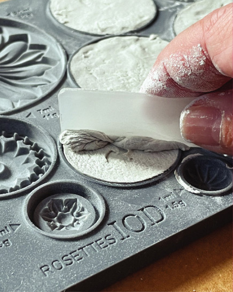 Hand smoothing white material into I.O.D. Rosettes Mould with scraper tool.