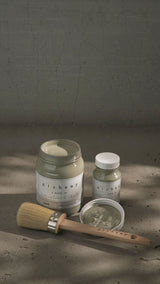 Three jars of Sage Alchemy Paint by Fusion Mineral Paint with a brush on a gray cracked surface.