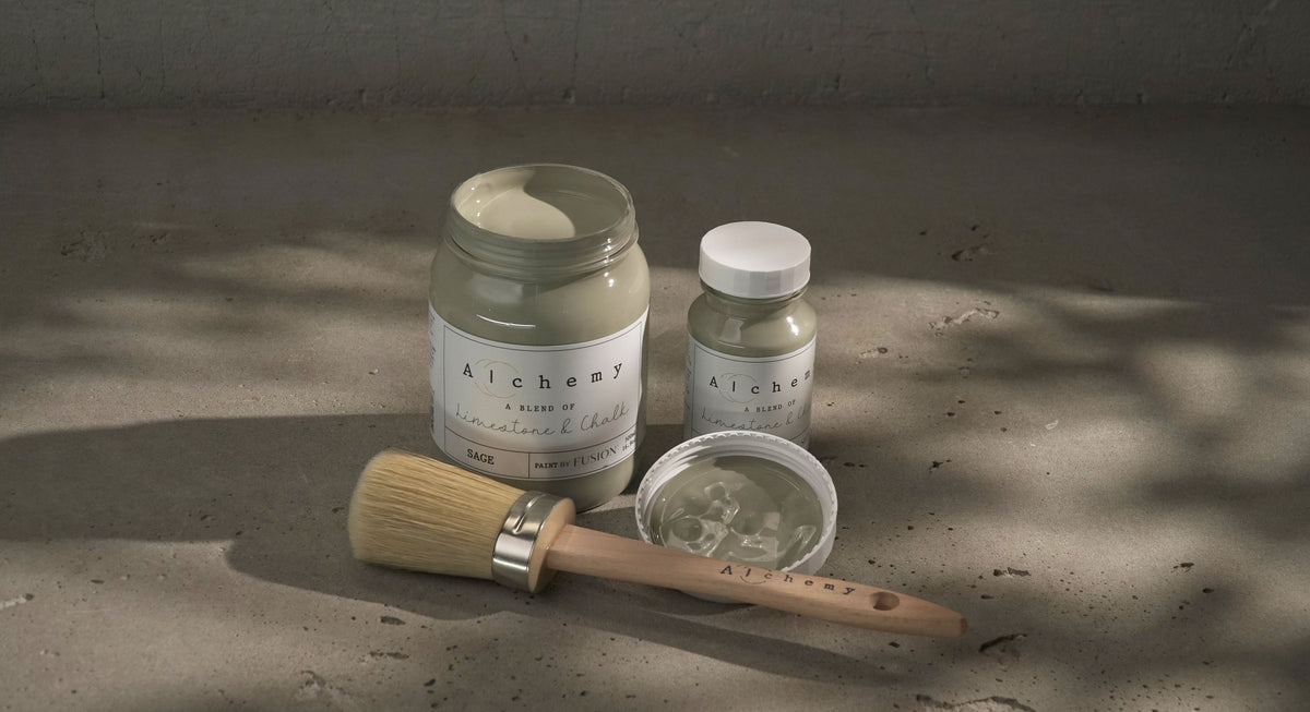 Sage Alchemy Paint by Fusion Mineral Paint open with brush, beside a jar and small bottle on concrete.