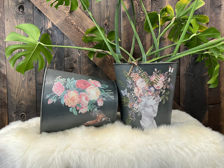 Two black pots with Saint Ouen Transfer by IOD; one pot contains a plant, displayed on a white furry surface.
