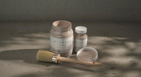 Three Sandstone Alchemy Paint by Fusion containers, one open with a brush, arranged on a textured surface.