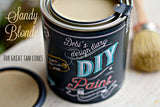 Open Sandy Blonde DIY Paint by DIY Paint Co., lid off, brush nearby, label reads “For Great Tan Lines.”.