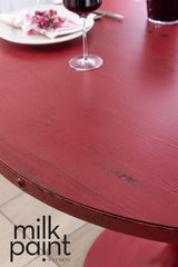 Distressed red round table in Sangria Milk Paint by Fusion Mineral Paint, set with wine, plate, cutlery, and flowers.