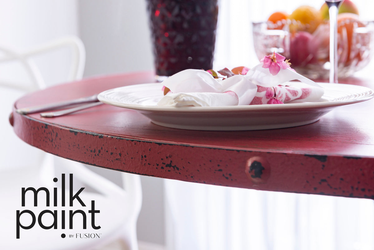 Weathered red table with white plate and napkin; Fusion Mineral Paint Sangria Milk Paint name in corner.